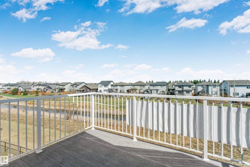 Deck featuring composite wood-finish flooring and white metal railings overlooking a landscaped green space and pond - 34 Harley Way, Spruce Grove, AB - Outdoor