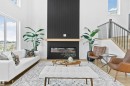 Double-height living space featuring large windows, wood-finish flooring, a contemporary linear fireplace with a black paneled surround, and an open staircase with black iron balusters - 34 Harley Way, Spruce Grove, AB  - Indoor Photo Showing Living Room With Fireplace 
