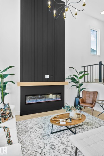 Soaring ceilings showcasing a striking floor-to-ceiling black paneled fireplace with a natural wood mantel - 34 Harley Way, Spruce Grove, AB - Indoor Photo Showing Other Room With Fireplace