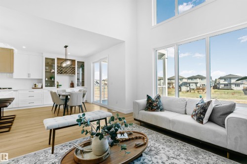 Double-height living space featuring expansive windows, light wood-finish flooring, and crisp white walls - 34 Harley Way, Spruce Grove, AB - Indoor Photo Showing Living Room