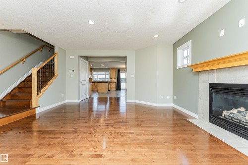 Open-concept living space featuring wood-finish flooring, a contemporary fireplace with a light-colored tile surround and wooden mantel, and a staircase with wood treads and balusters - 8530 76 Avenue, Edmonton, AB - Indoor Photo Showing Other Room With Fireplace