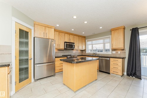 Kitchen featuring light wood cabinetry, granite-style countertops, stainless steel appliances, and a central island - 8530 76 Avenue, Edmonton, AB - Indoor Photo Showing Kitchen