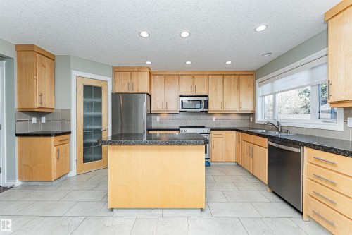 Kitchen featuring light wood cabinetry, dark speckled countertops, tile backsplash, stainless steel appliances, and recessed lighting - 8530 76 Avenue, Edmonton, AB - Indoor Photo Showing Kitchen With Double Sink