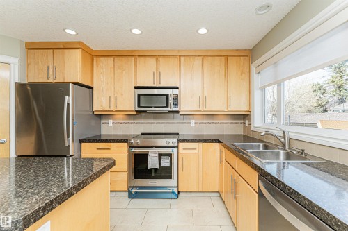 Kitchen featuring wood cabinetry, stainless steel appliances, dark speckled countertops, a tile backsplash, and recessed lighting - 8530 76 Avenue, Edmonton, AB - Indoor Photo Showing Kitchen With Double Sink
