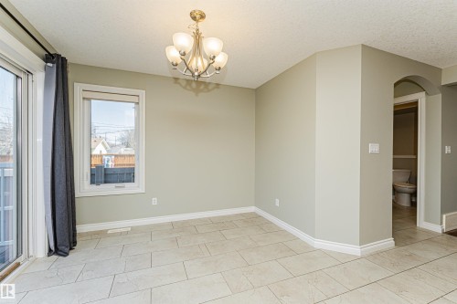 Spacious room featuring light-colored tile flooring, a modern chandelier, a large sliding glass door, and a single window - 8530 76 Avenue, Edmonton, AB - Indoor Photo Showing Other Room