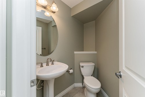 Pedestal sink with brushed nickel faucet, oval mirror, and three-light vanity fixture - 8530 76 Avenue, Edmonton, AB - Indoor Photo Showing Bathroom