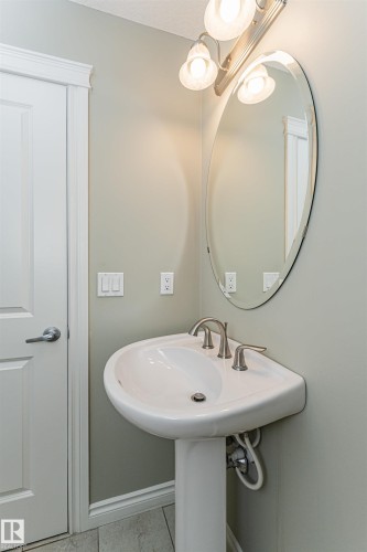 Pedestal sink with brushed nickel faucet, illuminated by a three-light vanity fixture - 8530 76 Avenue, Edmonton, AB - Indoor Photo Showing Bathroom