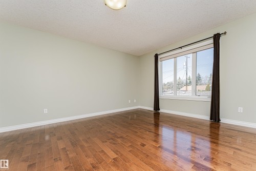 Spacious interior featuring wood-finish flooring, a large multi-pane window, light-toned walls, white baseboards, and a ceiling-mounted light fixture - 8530 76 Avenue, Edmonton, AB - Indoor Photo Showing Other Room