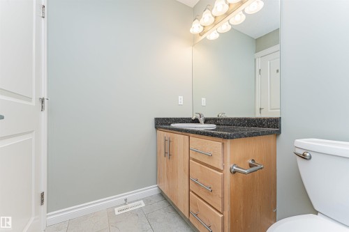 Bathroom featuring a wood-finish vanity with a dark countertop and integrated sink, under a mirrored wall with a multi-bulb light fixture - 8530 76 Avenue, Edmonton, AB - Indoor Photo Showing Bathroom