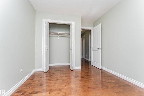 Interior room featuring wood-finish flooring, light green walls, a closet with bi-fold doors, and a white interior door - 8530 76 Avenue, Edmonton, AB - Indoor Photo Showing Other Room