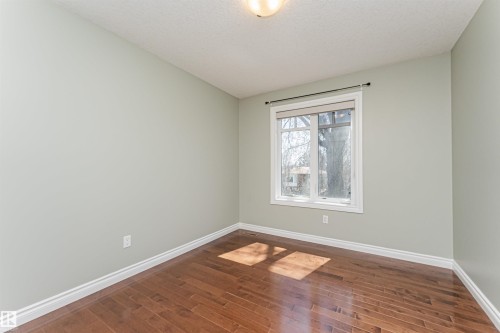Well-lit room with wood-finish flooring, light green walls, a window featuring white trim, and a ceiling light fixture - 8530 76 Avenue, Edmonton, AB - Indoor Photo Showing Other Room