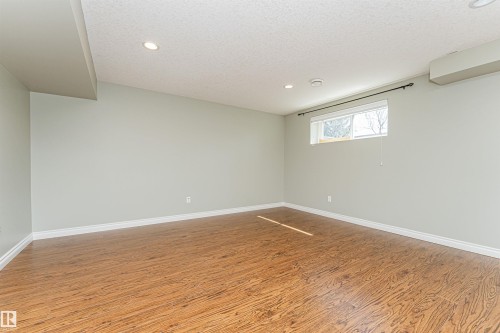 Spacious room featuring wood-finish flooring, light grey walls, recessed ceiling lighting, and a single window with a dark curtain rod - 8530 76 Avenue, Edmonton, AB - Indoor Photo Showing Other Room