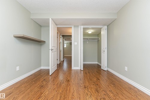 Room featuring wood-finish flooring, light green walls, a floating shelf, a closet with bi-fold doors, and a paneled interior door - 8530 76 Avenue, Edmonton, AB - Indoor Photo Showing Other Room