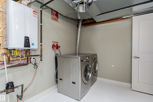 Utility space featuring a tankless water heater, exposed piping, and a white interior door with contemporary hardware - 8530 76 Avenue, Edmonton, AB - Indoor Photo Showing Laundry Room