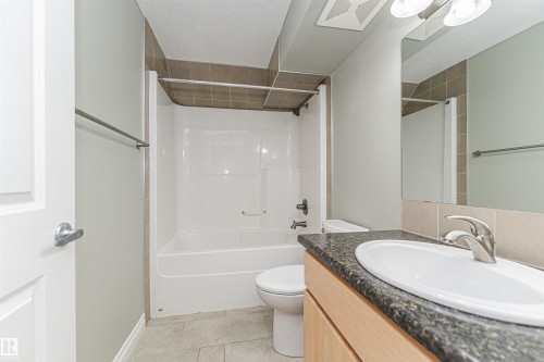 Bathroom featuring a white tub/shower combination, light-colored wall tile, and a light wood-finish vanity with a dark speckled countertop and undermount sink - 8530 76 Avenue, Edmonton, AB - Indoor Photo Showing Bathroom
