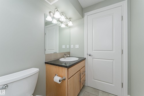 Bathroom featuring a light wood-finish vanity with a dark speckled countertop, undermount sink, and chrome faucet - 8530 76 Avenue, Edmonton, AB - Indoor Photo Showing Bathroom