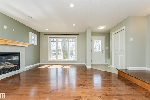 Living area featuring wood-finish flooring, a fireplace with a light-colored stone surround and wood mantel, large window, additional windows, and recessed lighting - 8530 76 Avenue, Edmonton, AB - Indoor With Fireplace