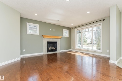 Spacious living area featuring wood-finish flooring, a stone-clad fireplace with a wood mantel, a large picture window, and recessed lighting - 8530 76 Avenue, Edmonton, AB - Indoor Photo Showing Living Room With Fireplace
