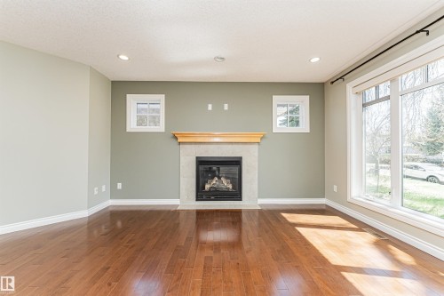 Central fireplace with light-toned tile surround and wood mantel - 8530 76 Avenue, Edmonton, AB - Indoor Photo Showing Other Room With Fireplace