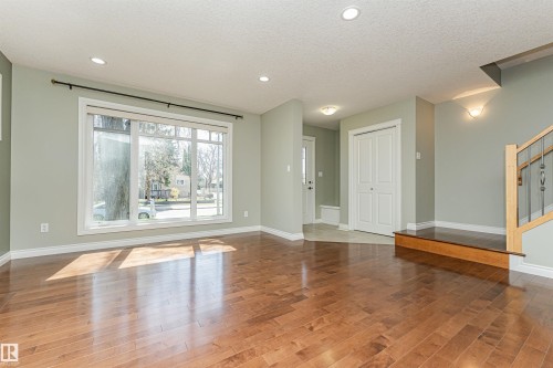 Expansive living area featuring wood-finish flooring, a large multi-pane window, recessed ceiling lighting, and a prominent staircase with wood and wrought iron balusters - 8530 76 Avenue, Edmonton, AB - Indoor Photo Showing Other Room