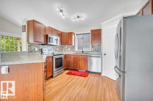 Kitchen featuring wood cabinetry, stainless steel appliances, speckled countertops, a tile backsplash, and wood-finish flooring - 21223 92 Avenue, Edmonton, AB - Indoor Photo Showing Kitchen