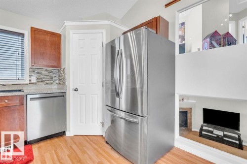 Kitchen with wood-finish flooring, stainless steel refrigerator and dishwasher, light-toned countertops, and a mosaic tile backsplash - 21223 92 Avenue, Edmonton, AB - Indoor Photo Showing Other Room