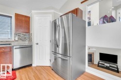 Kitchen with wood-finish flooring, stainless steel refrigerator and dishwasher, light-toned countertops, and a mosaic tile backsplash - 