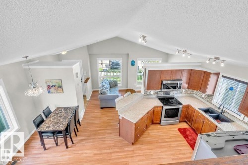Kitchen featuring wood-finish flooring, wood cabinetry, stone-finish countertops, stainless steel appliances, and a tiled backsplash - 21223 92 Avenue, Edmonton, AB - Indoor Photo Showing Kitchen With Double Sink