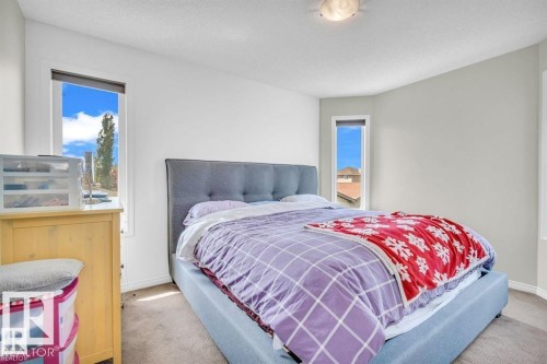 Corner bedroom featuring two vertical windows, light-toned walls, and neutral carpet flooring - 21223 92 Avenue, Edmonton, AB - Indoor Photo Showing Bedroom