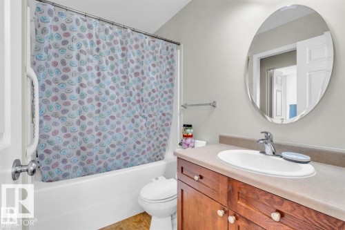 Bathroom featuring a white bathtub with a grab bar, a wood-finish vanity with a light-toned countertop, an oval-shaped mirror, and a chrome faucet - 21223 92 Avenue, Edmonton, AB - Indoor Photo Showing Bathroom