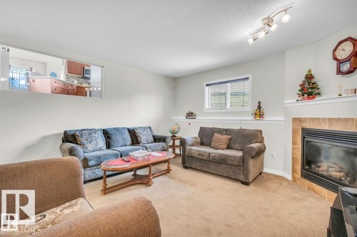 Spacious living area featuring neutral carpeting, a tiled fireplace with mantel, and a dedicated pass-through window to the kitchen - 21223 92 Avenue, Edmonton, AB - Indoor Photo Showing Living Room With Fireplace