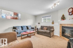 Spacious living area featuring neutral carpeting, a tiled fireplace with mantel, and a dedicated pass-through window to the kitchen - 