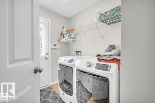 Dedicated laundry area featuring a white front-loading washer and dryer, wood-finish flooring, overhead wire shelving, and a glass-paneled exterior door with blinds - 21223 92 Avenue, Edmonton, AB - Indoor Photo Showing Laundry Room