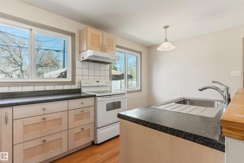 Kitchen featuring light wood cabinetry, dark speckled countertops, white tiled backsplash, and wood-finish flooring - 10620 68 Avenue, Edmonton, AB - Indoor Photo Showing Kitchen