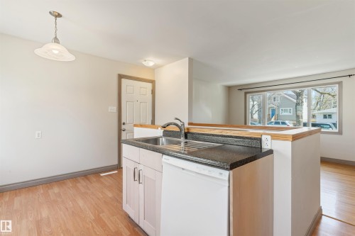 Kitchen featuring wood-finish flooring, a stainless steel sink, dark countertops, light-toned cabinetry, and a built-in dishwasher - 10620 68 Avenue, Edmonton, AB - Indoor Photo Showing Kitchen