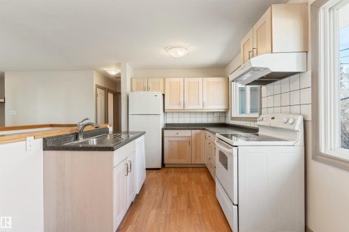 Kitchen featuring wood-finish flooring, light wood cabinetry, white appliances, dark countertops, and a white tiled backsplash - 10620 68 Avenue, Edmonton, AB - Indoor Photo Showing Kitchen With Double Sink