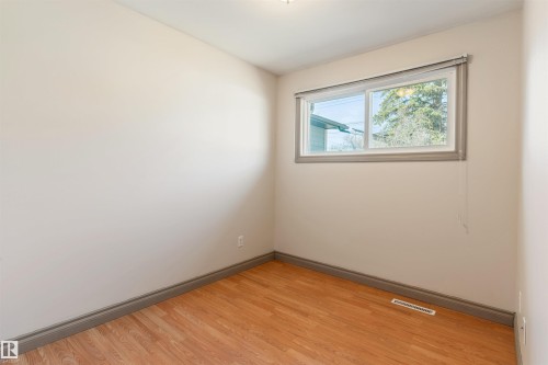 Room featuring a window with a roller blind, light tone walls, wood-finish flooring, and grey baseboards - 10620 68 Avenue, Edmonton, AB - Indoor Photo Showing Other Room