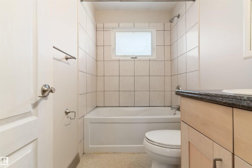 Full bathroom featuring a tub and shower combination with tile surround, a frosted window, and a light wood-finish vanity with a dark countertop and integrated sink - 10620 68 Avenue, Edmonton, AB - Indoor Photo Showing Bathroom
