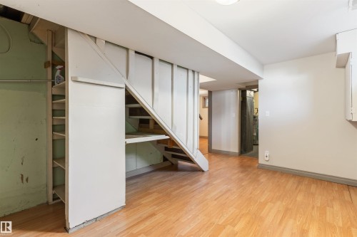 Open lower level area featuring wood-finish flooring, built-in shelving, and exposed ceiling joists - 10620 68 Avenue, Edmonton, AB - Indoor Photo Showing Other Room