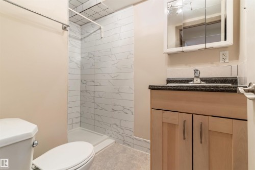 Bathroom featuring a stand-up shower with white subway tile surround, light wood-finish vanity with dark countertop, and a mirrored medicine cabinet - 10620 68 Avenue, Edmonton, AB - Indoor Photo Showing Bathroom