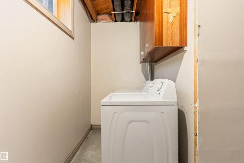 Dedicated laundry area featuring a top-loading washing machine, overhead wood-finish cabinetry, and a single window - 10620 68 Avenue, Edmonton, AB - Indoor Photo Showing Laundry Room