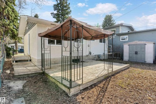 Expansive wood deck with a detached gazebo frame, offering direct access to the home's exterior with stucco siding and a built-in storage shed - 10620 68 Avenue, Edmonton, AB - Outdoor