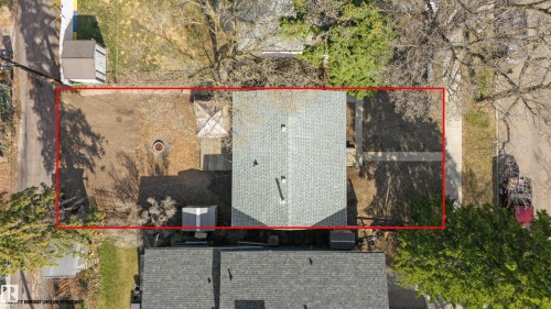 Aerial view showcasing the property's perimeter, featuring a gabled roof, an open lawn area with a fire pit, and mature trees providing natural shading - 10620 68 Avenue, Edmonton, AB - 