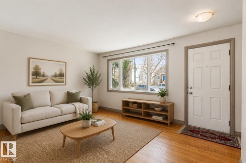 Bright living area featuring wood-finish flooring, a large multi-pane window, and a paneled entry door - 10620 68 Avenue, Edmonton, AB - Indoor Photo Showing Living Room