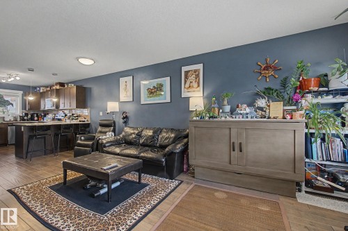 Open-concept living area featuring wood-finish flooring, a kitchen with dark cabinetry, and a central island with bar seating - 210 401 Southfork Drive, Leduc, AB - Indoor Photo Showing Living Room