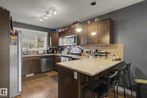 Kitchen featuring wood-finish flooring, dark wood cabinetry, stainless steel appliances, and light-toned countertops - 210 401 Southfork Drive, Leduc, AB - Indoor Photo Showing Kitchen