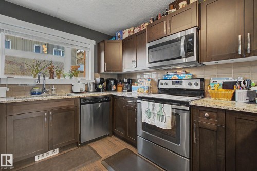 Kitchen featuring wood-finish cabinetry, granite-style countertops, stainless steel appliances, a tiled backsplash, and wood-finish flooring - 210 401 Southfork Drive, Leduc, AB - Indoor Photo Showing Kitchen