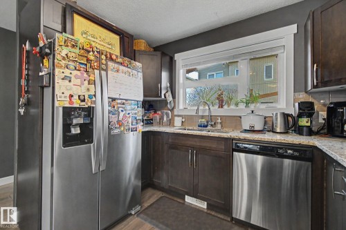 Kitchen featuring dark wood cabinetry, light speckled countertops, stainless steel appliances, and a window above the sink - 210 401 Southfork Drive, Leduc, AB - Indoor Photo Showing Kitchen