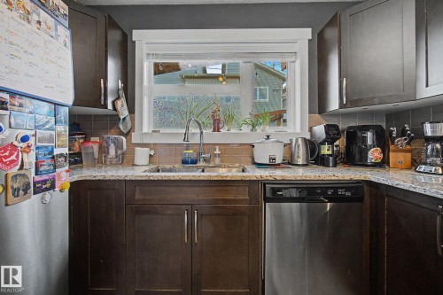 Kitchen featuring dark wood-finish cabinetry, light speckled countertops, and a tiled backsplash - 210 401 Southfork Drive, Leduc, AB - Indoor Photo Showing Kitchen With Double Sink