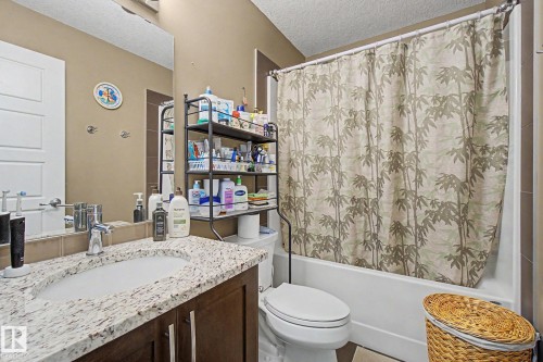 Bathroom featuring an integrated bathtub and shower, a single vanity with a stone-finish countertop, and a wood-finish cabinet - 210 401 Southfork Drive, Leduc, AB - Indoor Photo Showing Bathroom